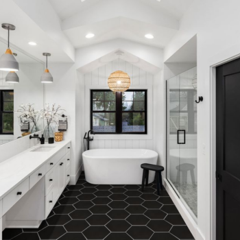 Farmhouse look bathroom with large black hexagon floor tiles, white tub, and white silestone countertop.