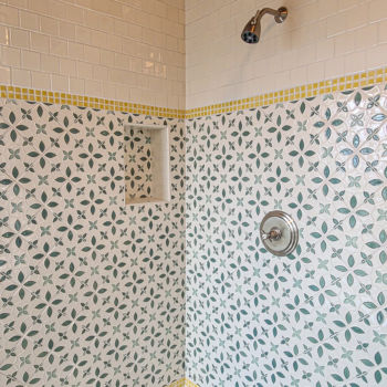 Green and white decorative shower wall with yellow trim. Small grey square floor tiles and wood ceiling with white subway tiles for additional trim.Tile installation by GWH Flooring store in Central Texas.
