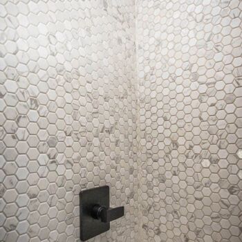 Hexagonal penny tile shower/bath wall. Variations in color from white to grey. Black square hardware. Tile Installation by GWH Flooring