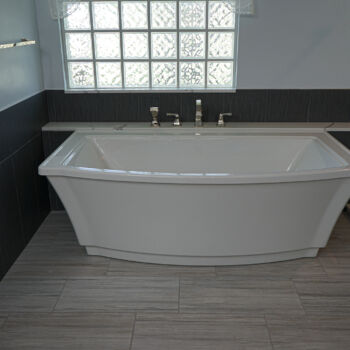 White quartz shelf iwth grey ribboning for a large bath tub. Large square dark grey wall tile, and grey wood grain floor tiles. Installation by GWH Flooring in Wimberley, Texas