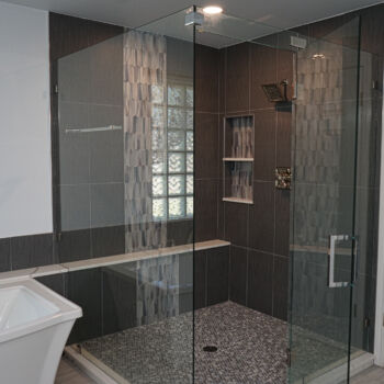 White quartz shelf with grey ribboning for a large bath tub. Large square dark grey wall tile, and grey wood grain floor tiles. Custom shower tiles include dark grey rectangular tiles, vertical ribbon of custom tile also used in niche. Quartz shelf goes all the way across for shower bench. Installation by GWH Flooring in Wimberley, Texas