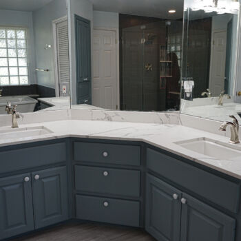 Corner vanity with quartz counter top that is white with grey ribbons. Cabinets are blue grey. Installation of counter tops by GWH Flooring store in Wimberley, Central Texas Hill Country