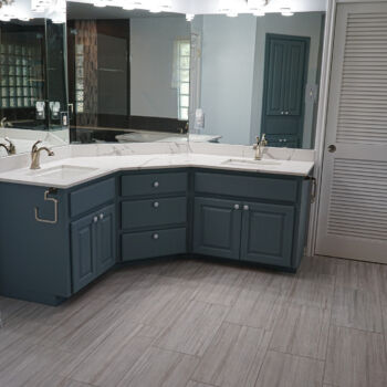 Corner vanity with quartz counter top that is white with grey ribbons. Cabinets are blue grey. Wood grain floor tiles. Installation of counter tops by GWH Flooring store in Wimberley, Central Texas Hill Country