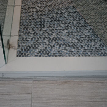 Blue penny round shower floor tiles with white quartz shower edge that has grey ribbons. Wood grain bathroom floor tile. Installed by GWH Flooring company in Dripping springs