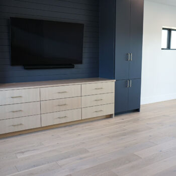 White oak floor installed in a media room with blue cabinets and slatted backing for TV. Installation in Driftwood by GWH Flooring company.