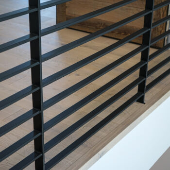 Edge of White Oak flooring looking over the ledge of a loft with black iron railing. Wood floor installed by GWH Flooring in Driftwood Central Texas.
