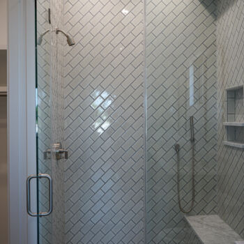White subway tiles installed on the diagonal in shower. Glass door, low bench, shower niche. Installation by GWH Flooring in Central Texas Hill Country