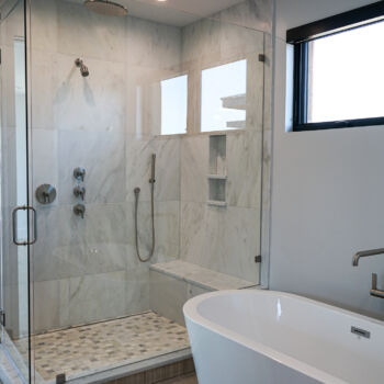 Quartz tiles in shower. Glass door, shower niche and bench. Wood tile floors in bathroom. White standalone tub. Installation by GWH Flooring in Central Texas Hill Country