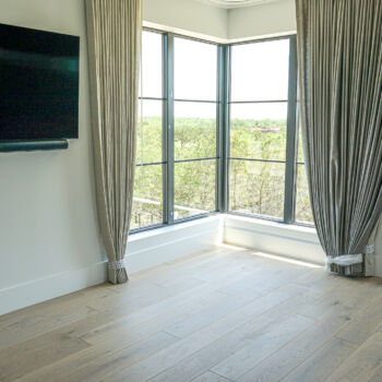 White Oak floor in bedroom with corner window. Heavy grey drapes and mounted television. Installation by GWH Flooring in Wimberley, Central Texas