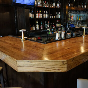 Custom wood bar installed by GWH Flooring Contractors in Buda, Texas. Liquor bottles in the background.