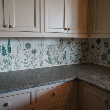 Custom floral green and white tile backplash and black and brown granite countertop in Wimberley kitchen. Installation by GWH Flooring company