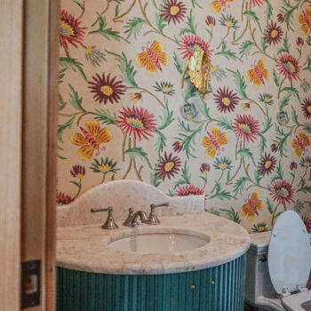 Custom marble counter top and blue vanity in bathroom with floral wallpaper and gold light sconces. Countertop installed by GWH Flooring