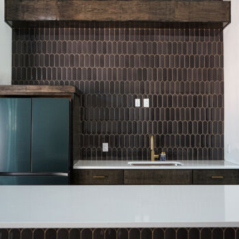 Counter to to peaked roof unique shaped dark tiles with gold grout. Custom floating wood shelves, white silestone countertops for sink and bar in commercial game room installed in Wimberley by GWH flooring