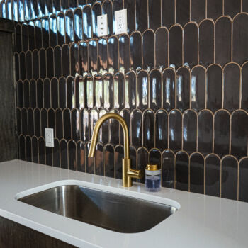 Counter to to peaked roof unique shaped dark tiles with gold grout. Custom floating wood shelves, white silestone countertops for sink and bar in commercial game room installed in Wimberley by GWH flooring