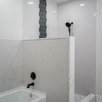 Grey and white honeycomb shaped bathroom tiles with silestone border and grey stripe from floor to ceiling. Standing shower with separate bath. Tile installation by GWH Flooring in Wimberley
