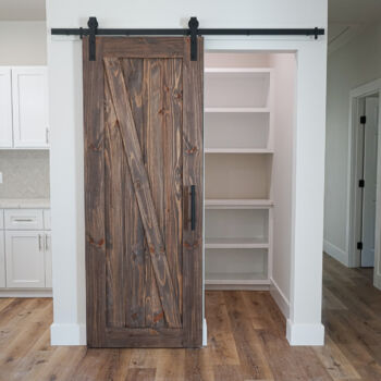 Wood floors in kitchen and pantry with a sliding wooden barn door. Floor installation by GWH Flooring in Wimberley