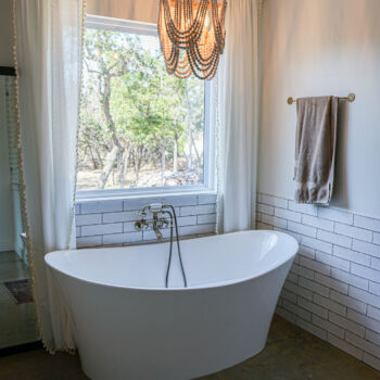 Beautiful bathroom with white subway tile "wainscoting" around the bathtub and a warm light chandelier. Tile installed by GWH Flooring in the Hill Country