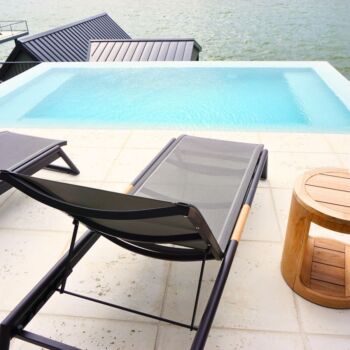 White limestone floor tiles surrounding pool that overlooks a lake in Texas. Black lounge chairs and wood table. Floor tile by GWH Flooring.