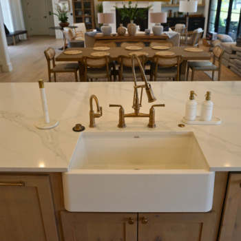 White Kitchen countertop, white oak wood floor, and white tile backsplash with brass faucet in Kingsland, Texas